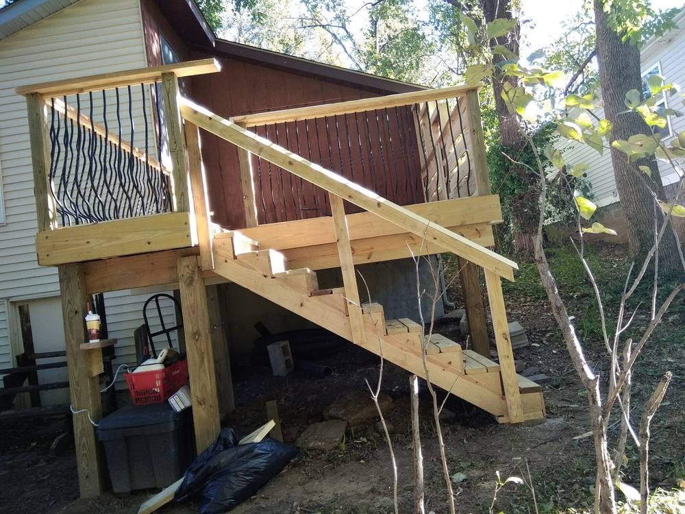 A new timber deck under construction behind a house, with framed railing posts, metal balusters and a run of stairs down to the yard, offcuts still on the ground.
