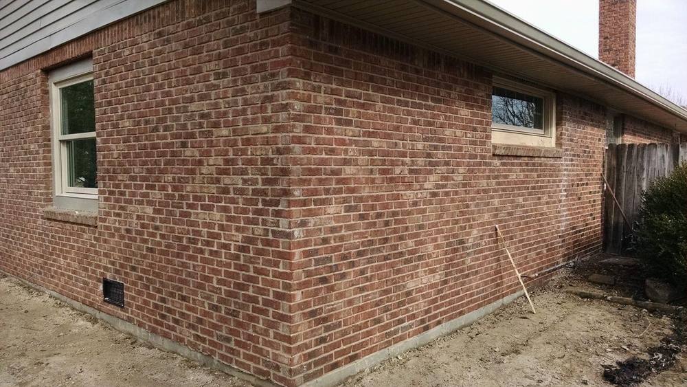 The rear brick corner of a single-storey house with fresh earth graded up to the foundation and new windows in place.